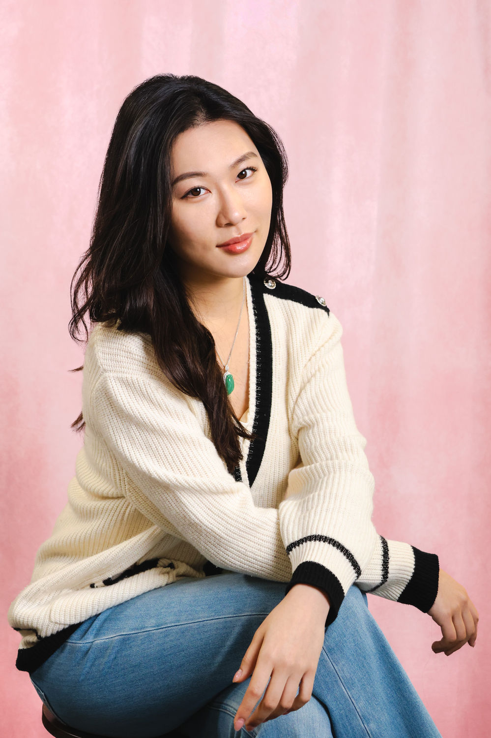 Relaxed seated portrait of a woman in a cream jumper against a soft pink backdrop at a London studio.