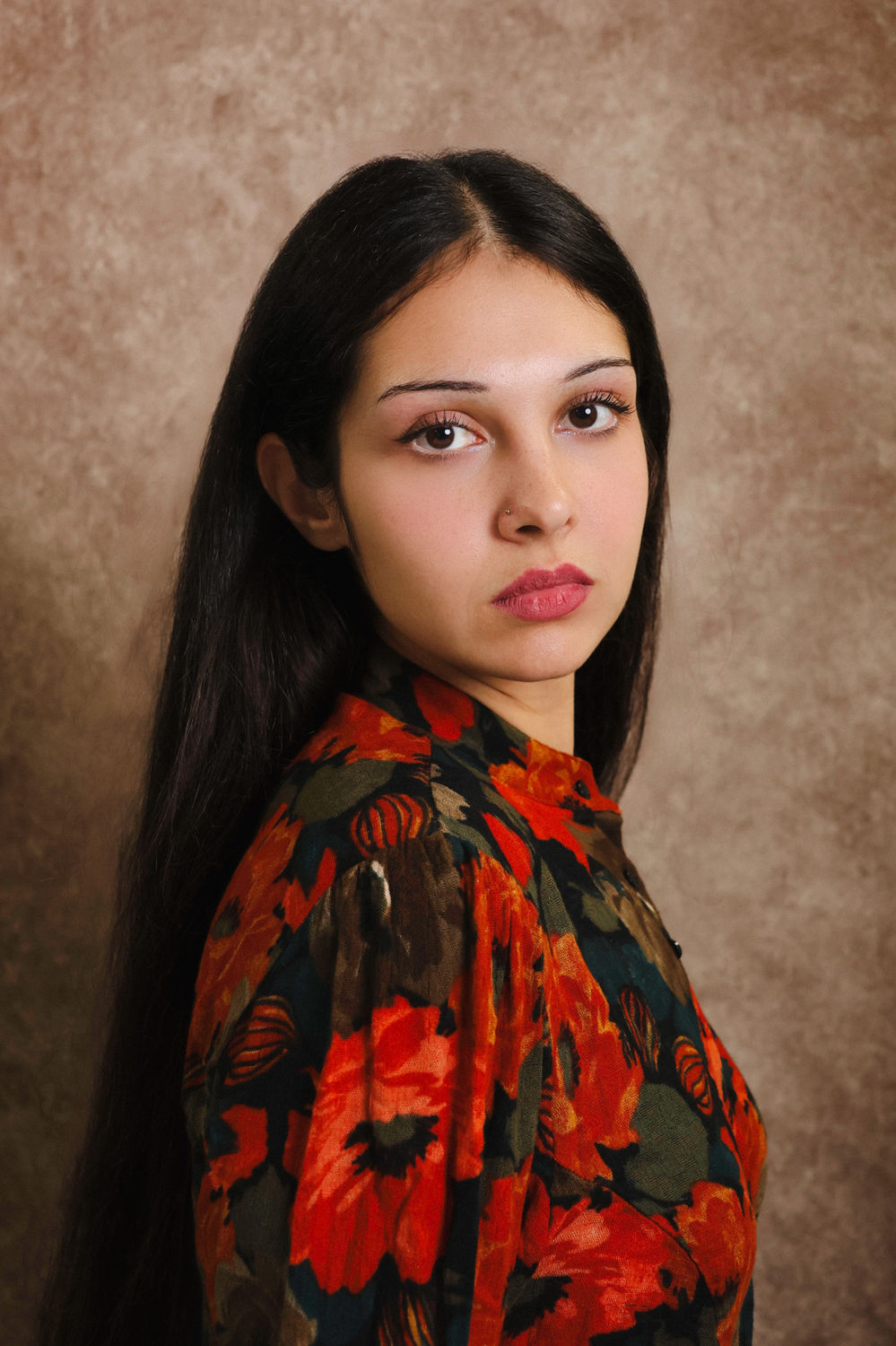 Editorial-style actor headshot of a person in a patterned top against a warm brown backdrop.