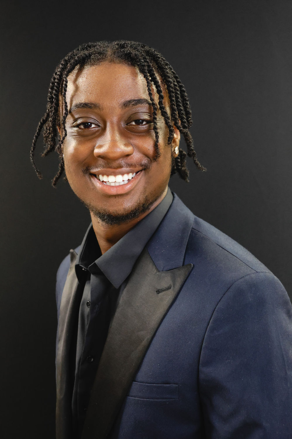 Modern portrait of a man in a dark jacket against a dark backdrop at a London creative studio.