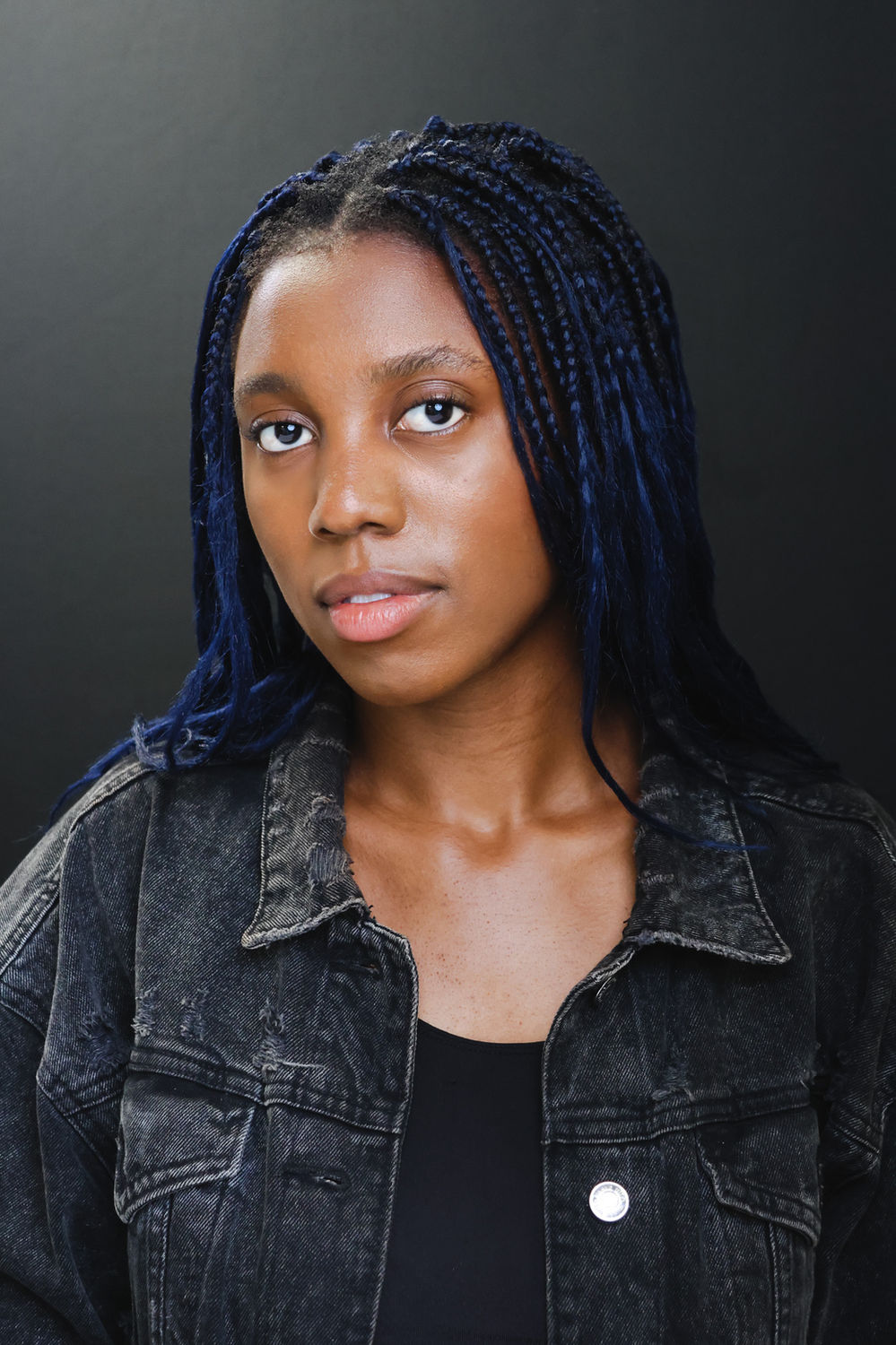Moody actor headshot of a person in a denim jacket against a black backdrop, suited to dramatic screen roles.