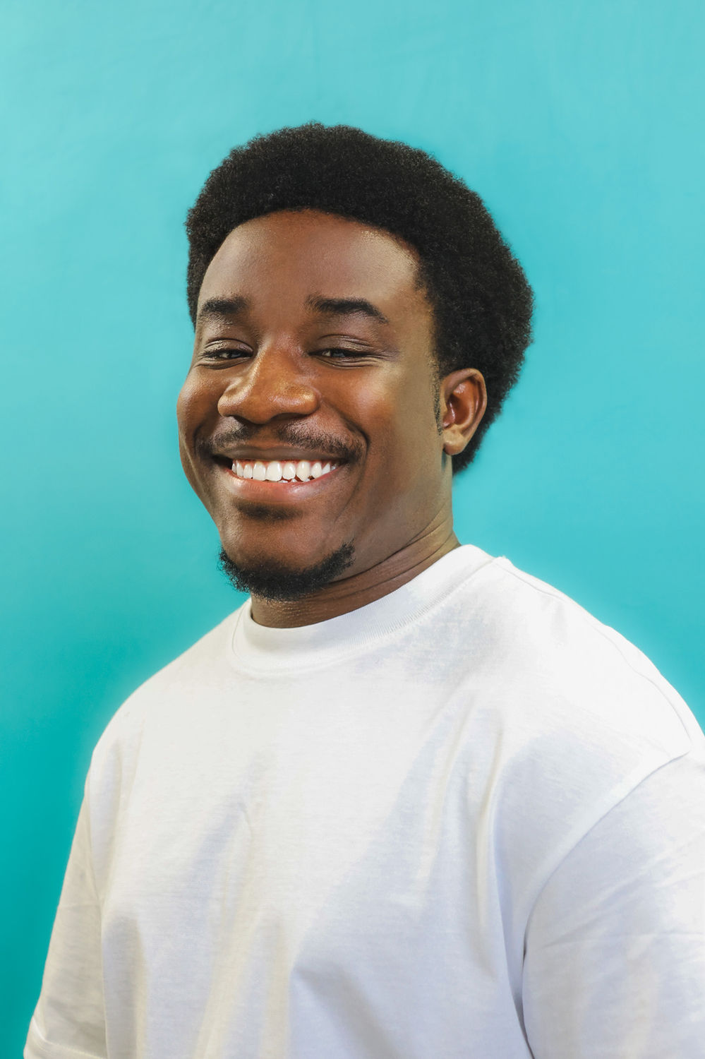 Bright commercial actor headshot of a smiling person in a white top against a bold blue backdrop, suited to advertising and lifestyle roles.