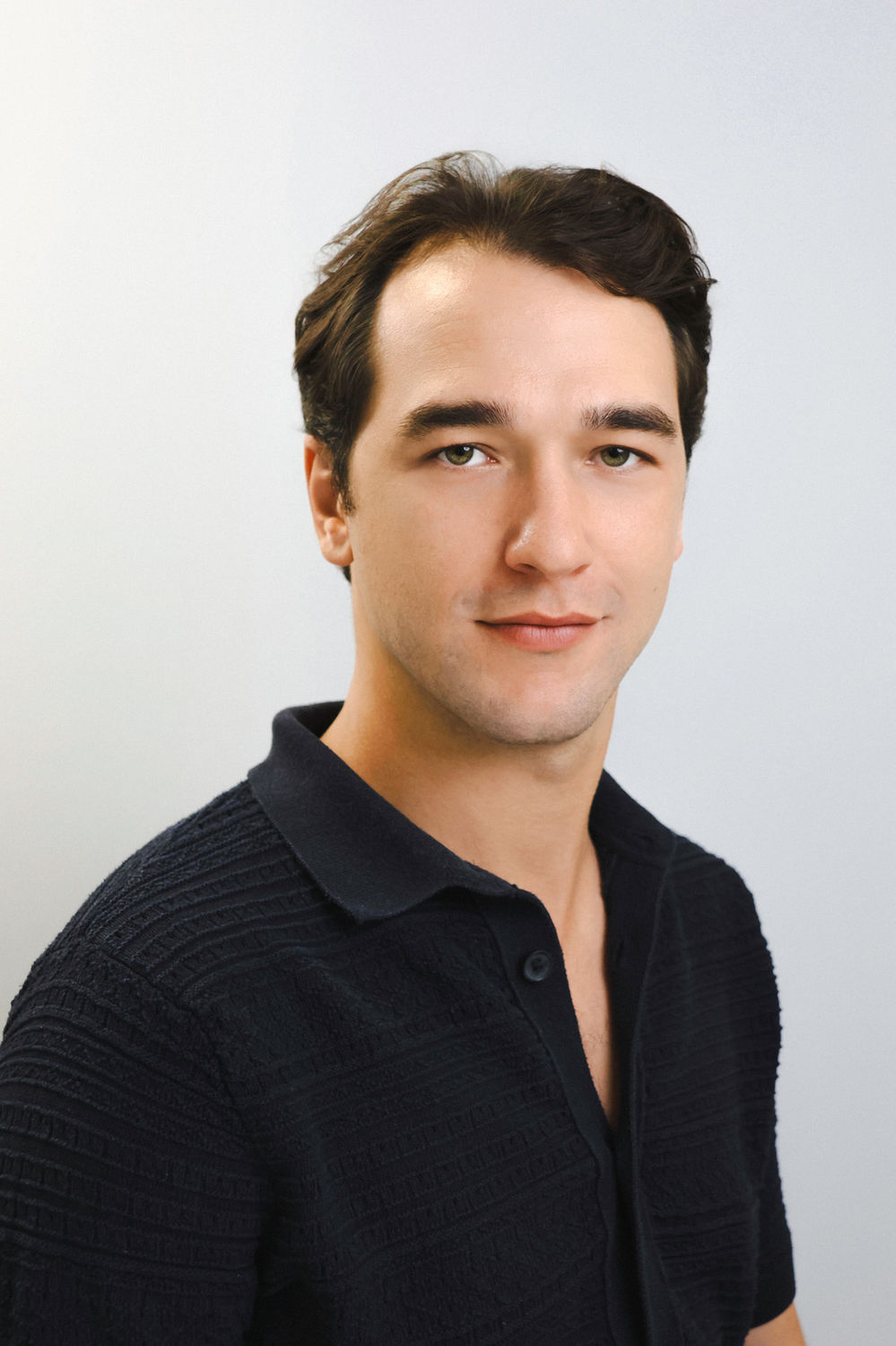 Smart-casual business portrait of a man in a dark polo shirt against a light studio backdrop, suited to LinkedIn profiles.