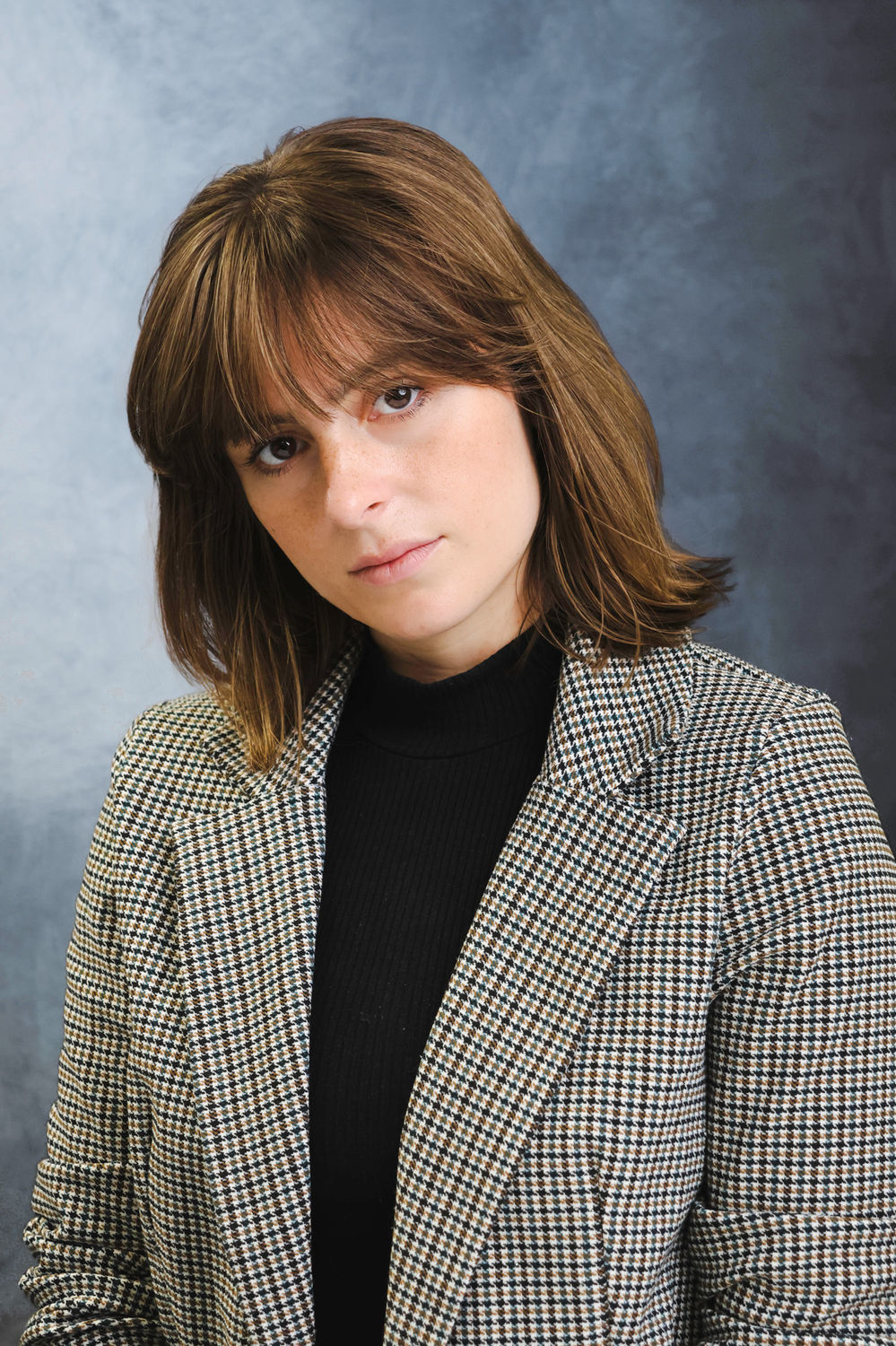 Professional portrait of a woman in a checked blazer against a neutral studio backdrop, suited to leadership and consultant profiles.