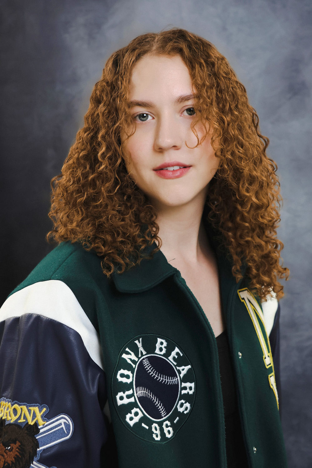Modern actor portrait of a person in a varsity-style jacket against a grey backdrop, suited to television and commercial casting.