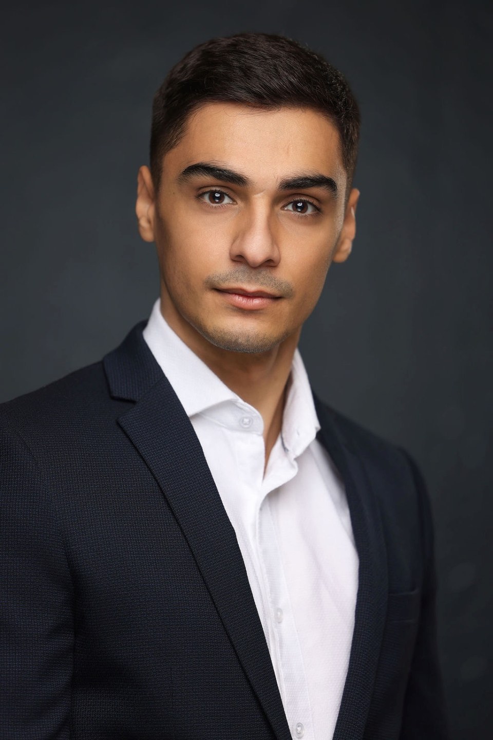 Classic business headshot in navy suit against charcoal backdrop